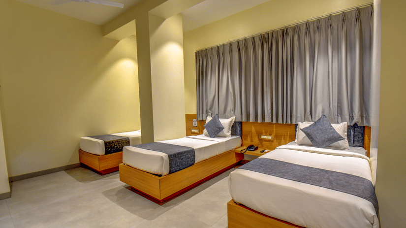 Deluxe Triple Room at VITS Select Nashik Hotels & Resorts featuring 3 single beds next to each other under warm lighting against a curtained window.
