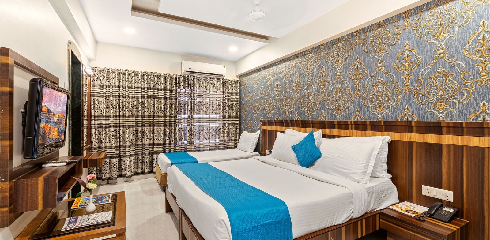 Spacious room at Mayur Retreat featuring a large double bed with turquoise throw and elegant blue wallpaper.