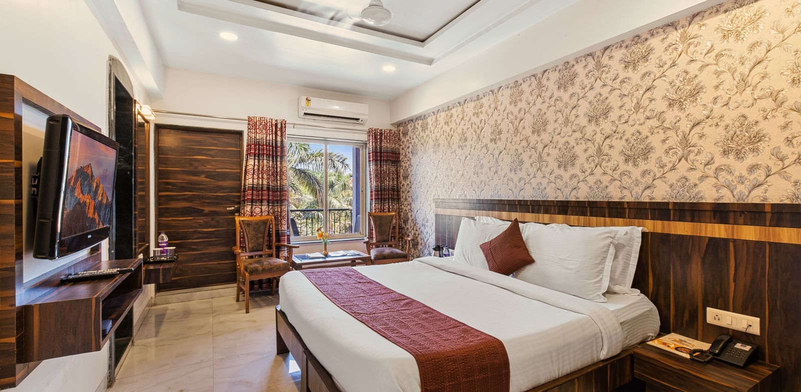 Warm-toned bedroom at Mayur Retreat with brown accents, floral wallpaper, and a scenic garden view.