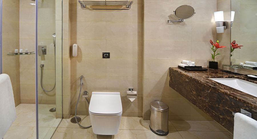 Modern bathroom with glass-enclosed shower, wall-mounted toilet, and elegant vanity at The Bristol Hotel, Gurgaon.