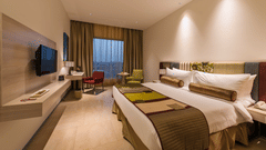 Contemporary guest room with twin beds, wall-mounted television, work desk and large window at Pride Elite Phaltan.