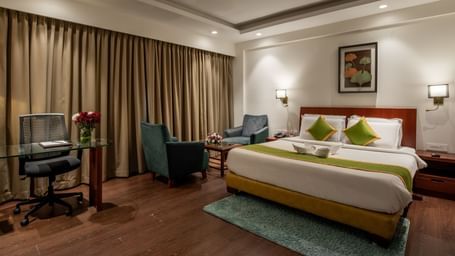 Bedroom with work desk, armchairs, and elegant curtains at Hotel Royal Regency Chennai
