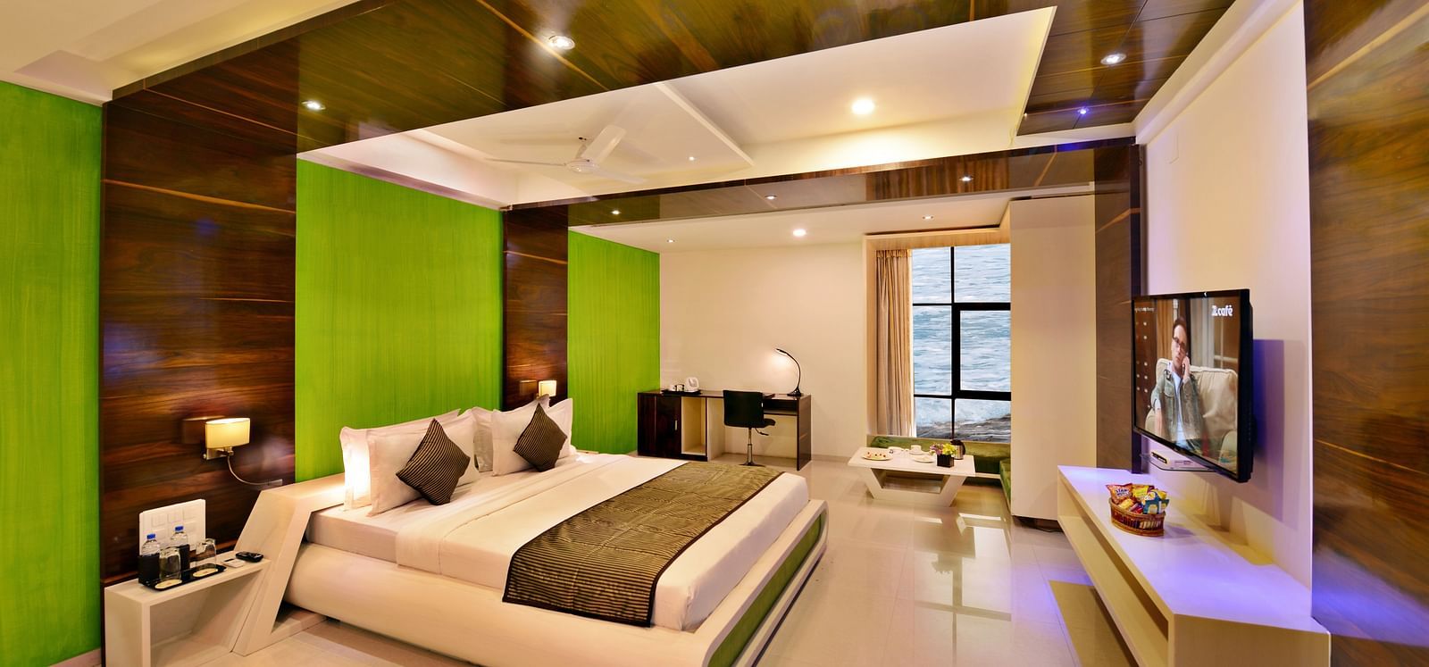 A stylish hotel room at Lords Inn Porbandar, features a king size bed with a green accent wall and modern furnishings.