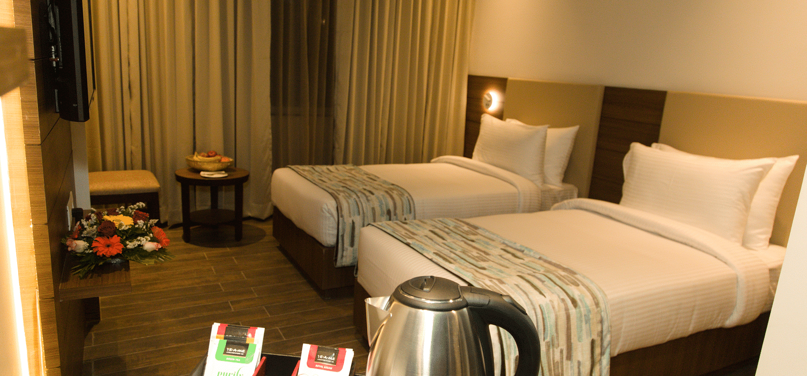 A hotel room at Lords Inn Udaipur offers two single beds with white linens, a kettle, cups, and tea bags on a counter.