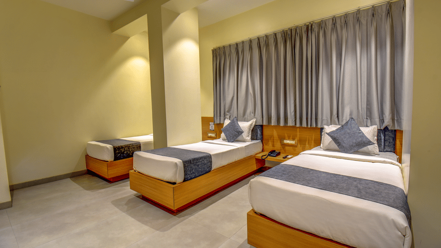 Delxue Triple Room at VITS Select Nashik Hotels & Resorts featuring 3 single beds next to each other under warm lighting against a curtained window