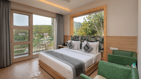 Premium Room at DLS Whispering Winds, Kasauli featuring a king size bed, accent seating, and large windows overlooking the valley.