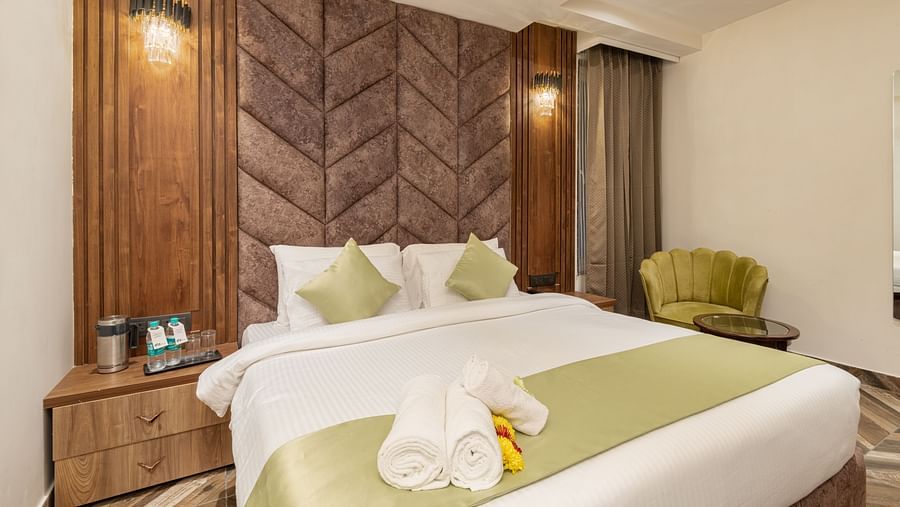 Image of Deluxe Room at DLS Grand Luxotica, Dehradun featuring a plush bed with rolled bath towels placed on the bed runner and a sitting space with a teapoy and couch next to it