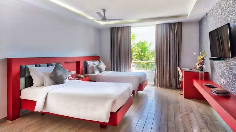 A hotel bedroom with two beds, each with red pillows, and modern red and grey furniture, under a bright ceiling  | Grand Chalet Twin | Grand Bay Resort and Spa
