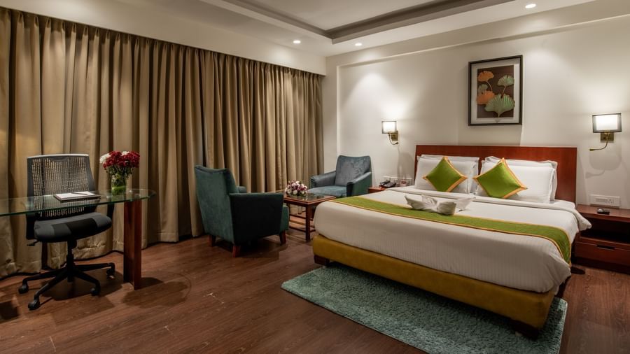 Bedroom with work desk, armchairs, and elegant curtains at Hotel Royal Regency Chennai