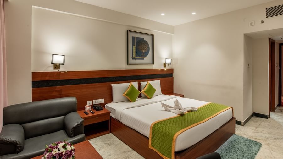 Bedroom featuring a comfortable bed, armchair, and warm lighting at Hotel Royal Regency Chennai