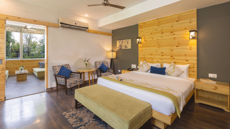 bedroom featuring a large bed with a decorative headboard, a seating area with chairs, and access to a balcony  at The Golden Tusk, Jim Corbett
