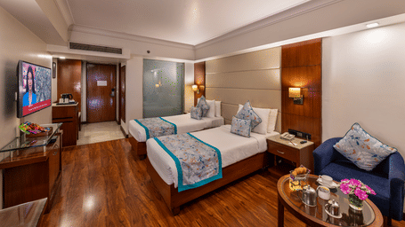 Deluxe twin bedroom with wooden flooring, flat screen TV, sitting area and bright lighting Lords Plaza Jaipur.