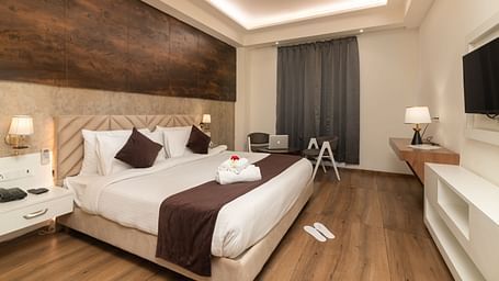 An image of a deluxe room with a work desk, chair, bed, flat screen TV, and other room amenities - DLS Ganga Bliss, Haridwar