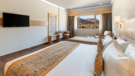 A close-up shot of a bed with a patterned runner on it and a tv mounted on the wall - Via Lakhela Resort & Spa, Kumbhalgarh