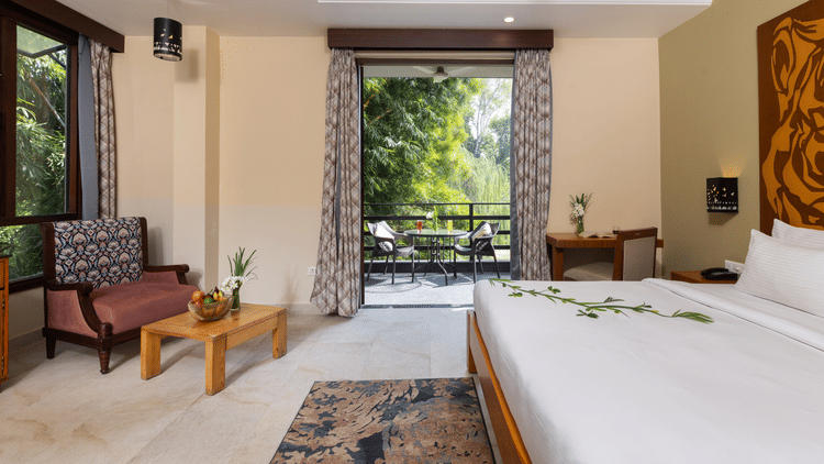  bedroom with a large bed, a seating area, and an open view to an outdoor patio  at The Golden Tusk, Jim Corbett