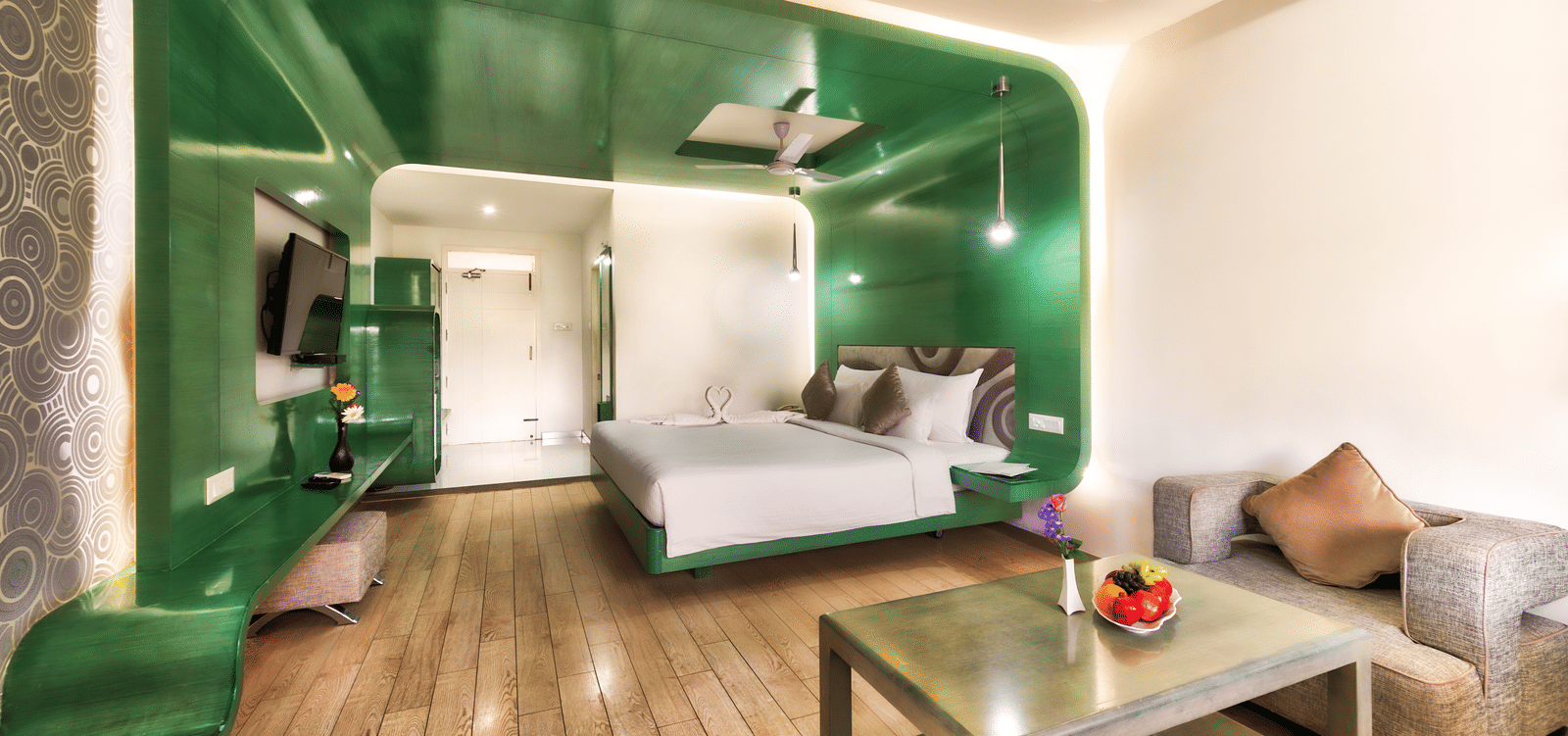 A room with king size bed, green glossy wall panel, and wooden furniture featuring a seating space at Grande Bay Resort & Spa, Mamallapuram.