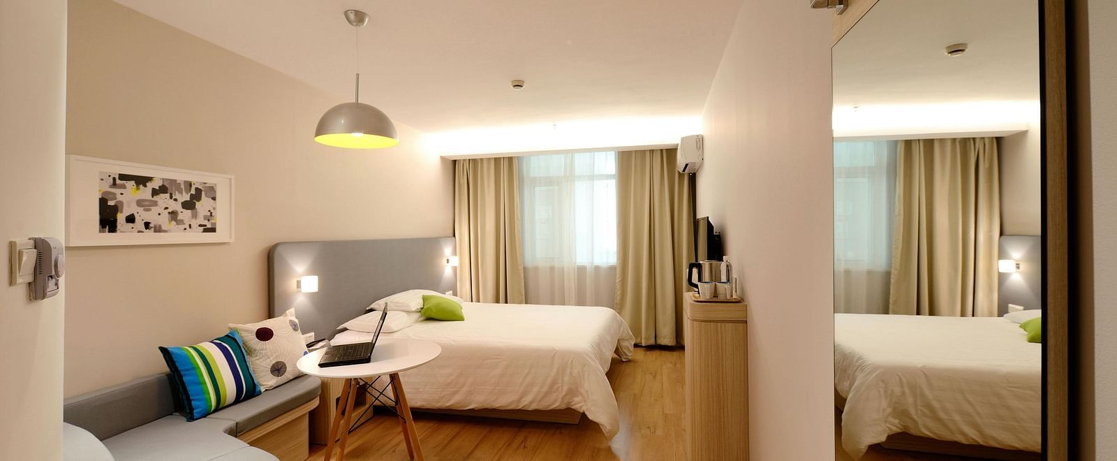 A bright hotel suite includes a seating area and a bed, reflected in a large mirror.
