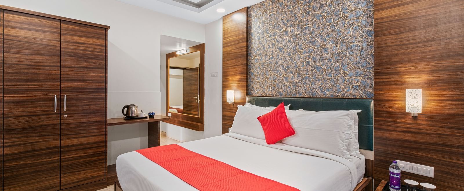 Well-furnished room at Mayur Retreat with a red-accented bed, wooden wardrobe, and soft lighting.