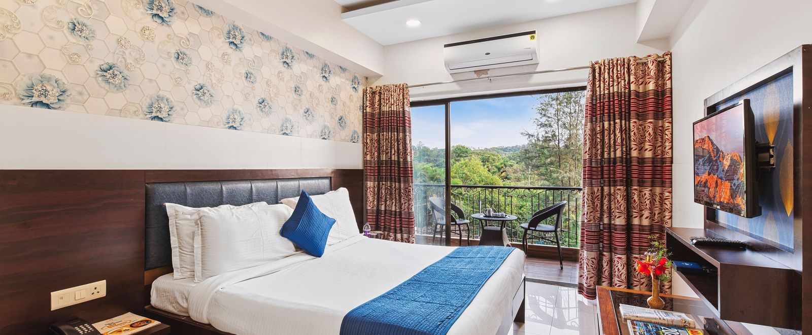 Bright and ventilated room at Mayur Retreat with a blue-themed bed, floral walls, and balcony garden view.