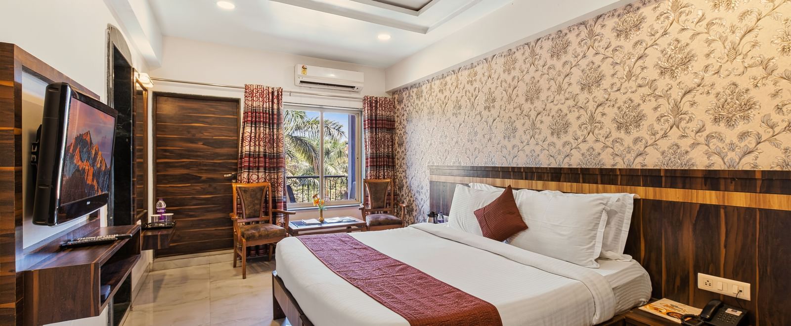 Warm-toned bedroom at Mayur Retreat with brown accents, floral wallpaper, and a scenic garden view.