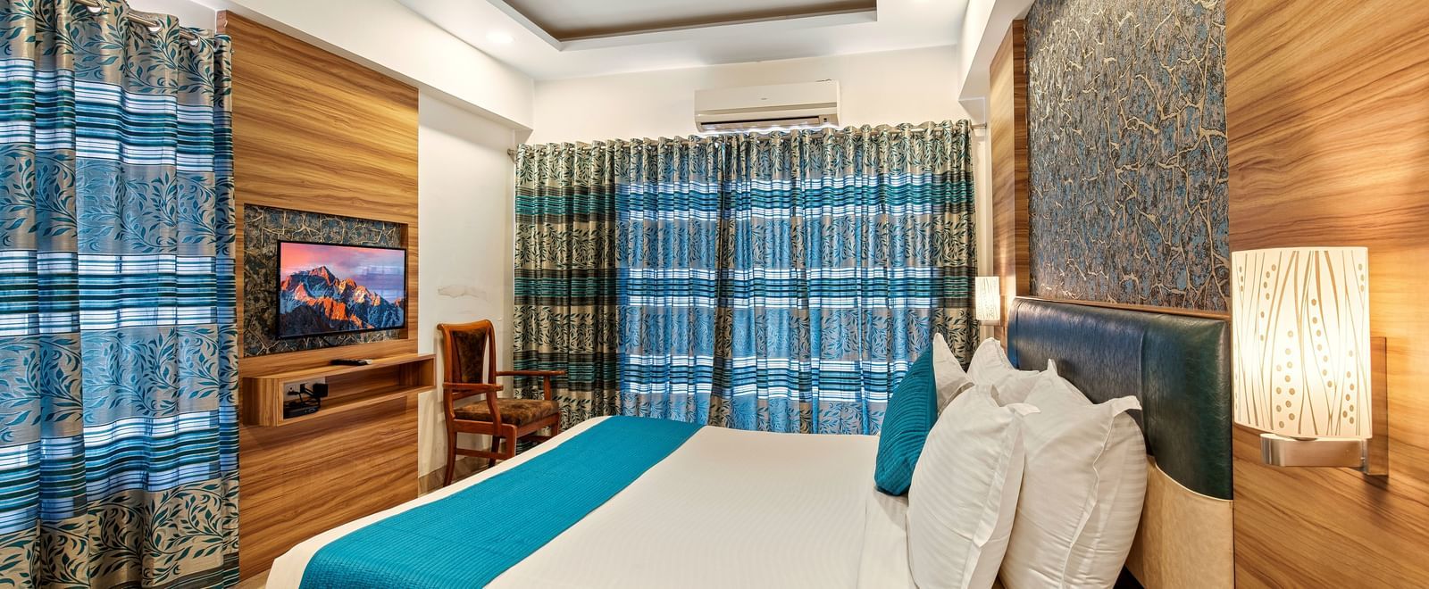 Cosy bedroom at Mayur Retreat with a blue-accented bed, wood paneling, and a wall-mounted TV.