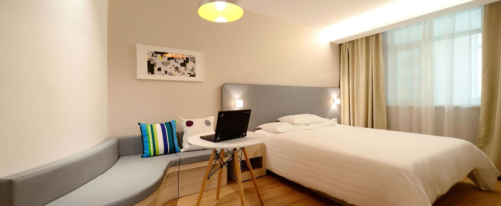 A compact hotel room with a neatly made bed, wooden flooring, and soft lighting.