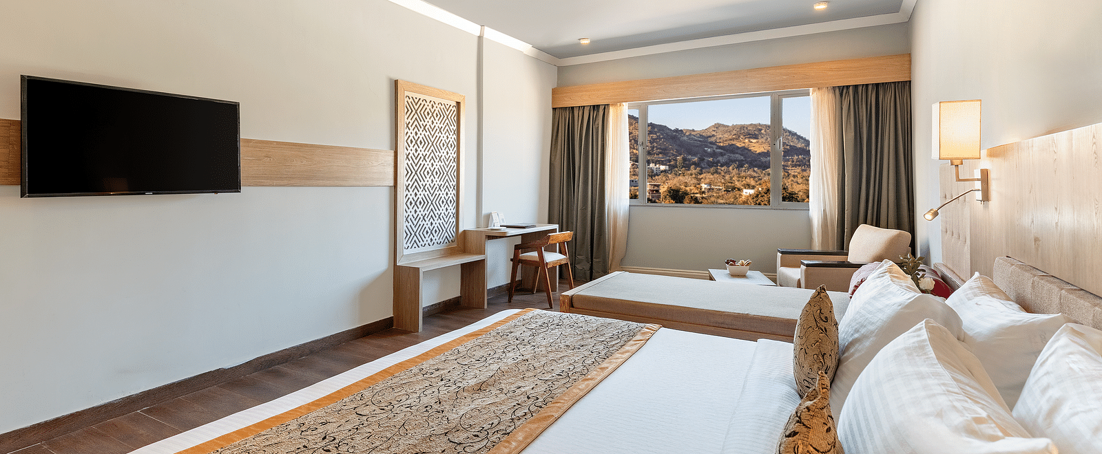 A close-up shot of a bed with a patterned runner on it and a tv mounted on the wall - Via Lakhela Resort & Spa, Kumbhalgarh