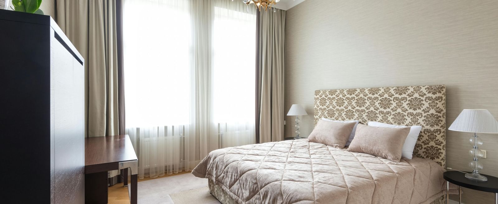 A bedroom features a patterned bedspread, neutral walls, and a chandelier.