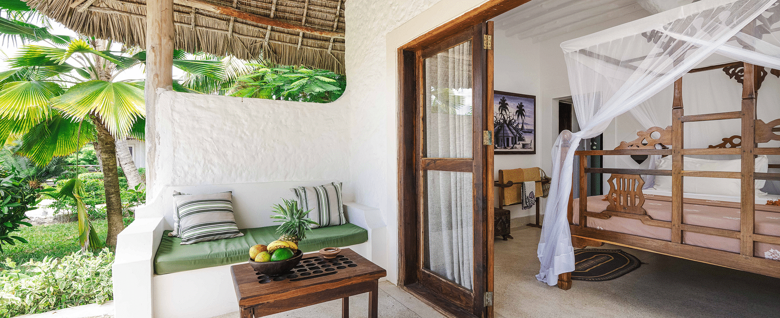A private patio at a tropical resort with white walls, a thatched roof, and a view into a bedroom with a four-poster bed - Shooting Star Boutique Hotel.