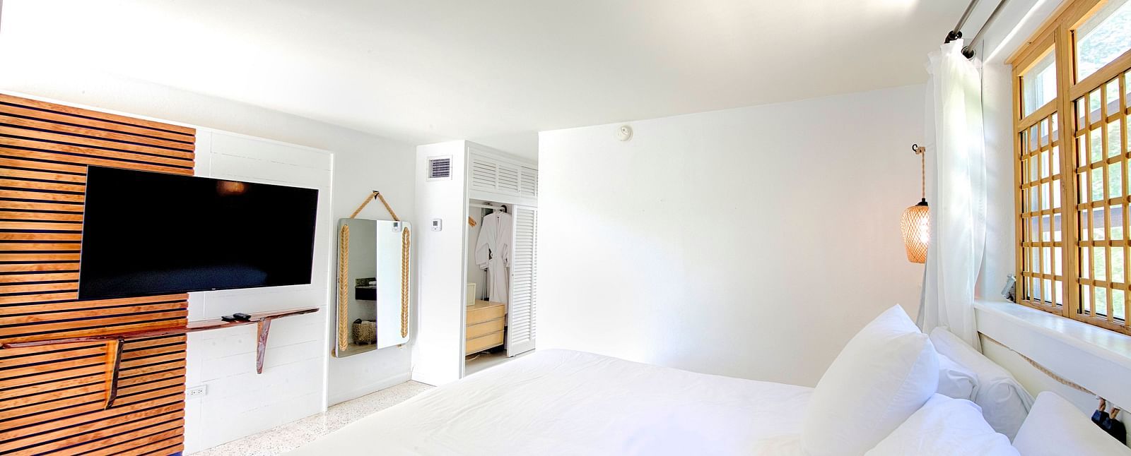 Bright bedroom at Casa Morada featuring a white bed, wall-mounted TV, and sliding wooden doors.