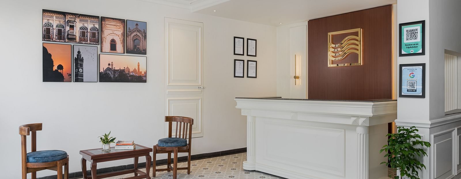 Reception area features a large desk with wall-mounted photo frames, and a pair of wooden chairs and a table in the middle | Hotel Ganga Maiya