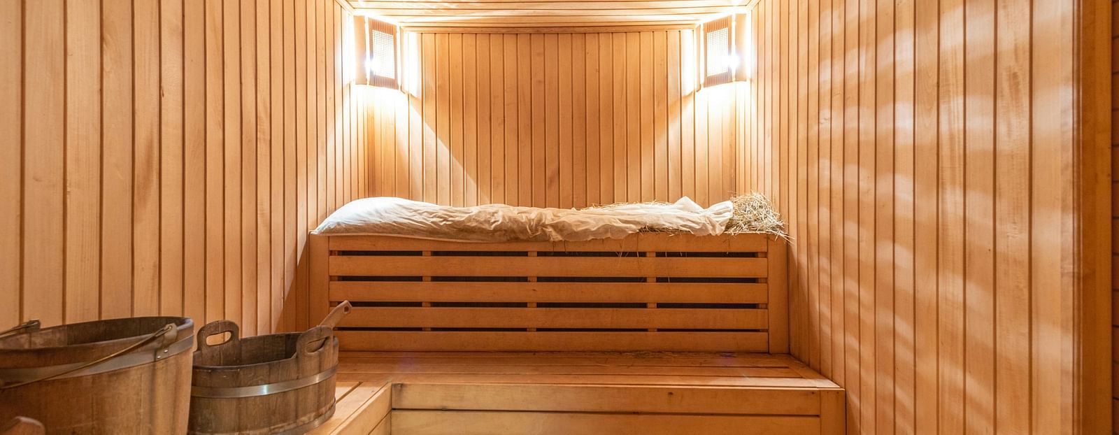 A wooden sauna room with two warm lights mounted in the corner of the ceilings.