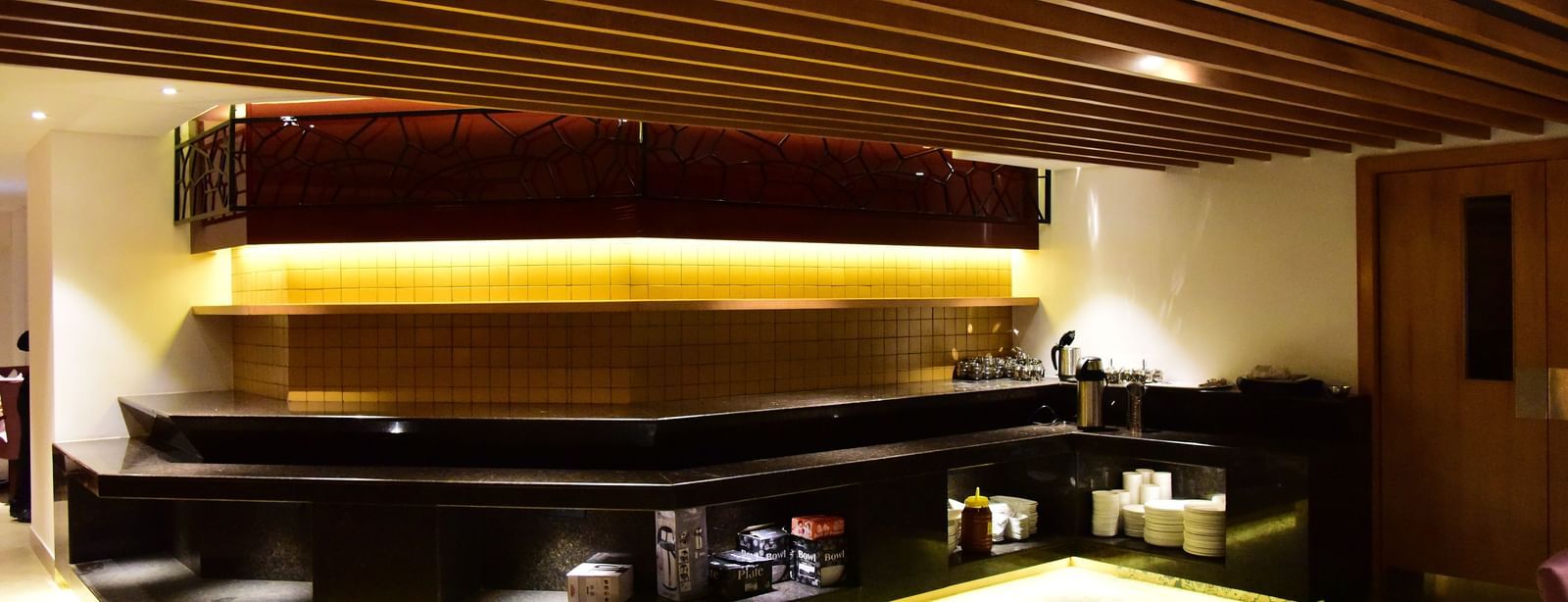 A long shot of the elegant restaurant and bar area at The Royal Comfort, showcasing a long bar with accent lighting and a cozy dining space with tables set for guests.