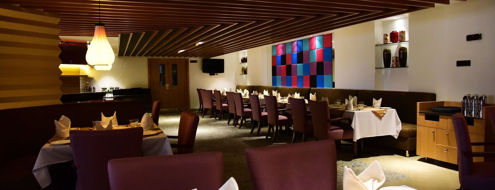 A side-angle shot of a hotel restaurant at The Royal Comfort, with elegant lighting, tables set for dinner, and a warm atmosphere.
