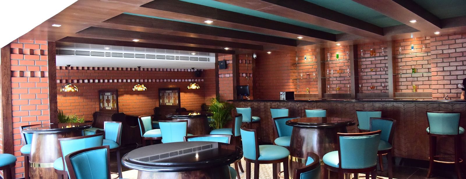 A close-up of the bar area at The Royal Comfort, with wooden rafters on the ceiling and a focus on the blue-green seating and intricate lighting fixtures.
