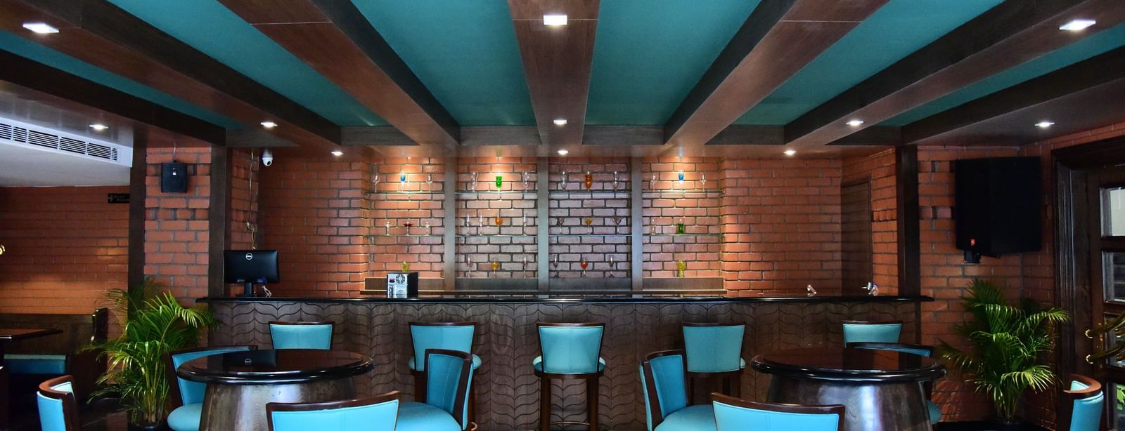 Another view of the bar at The Royal Comfort, highlighting the long wooden bar top, the brick wall behind it, and the stylish blue-green chairs.