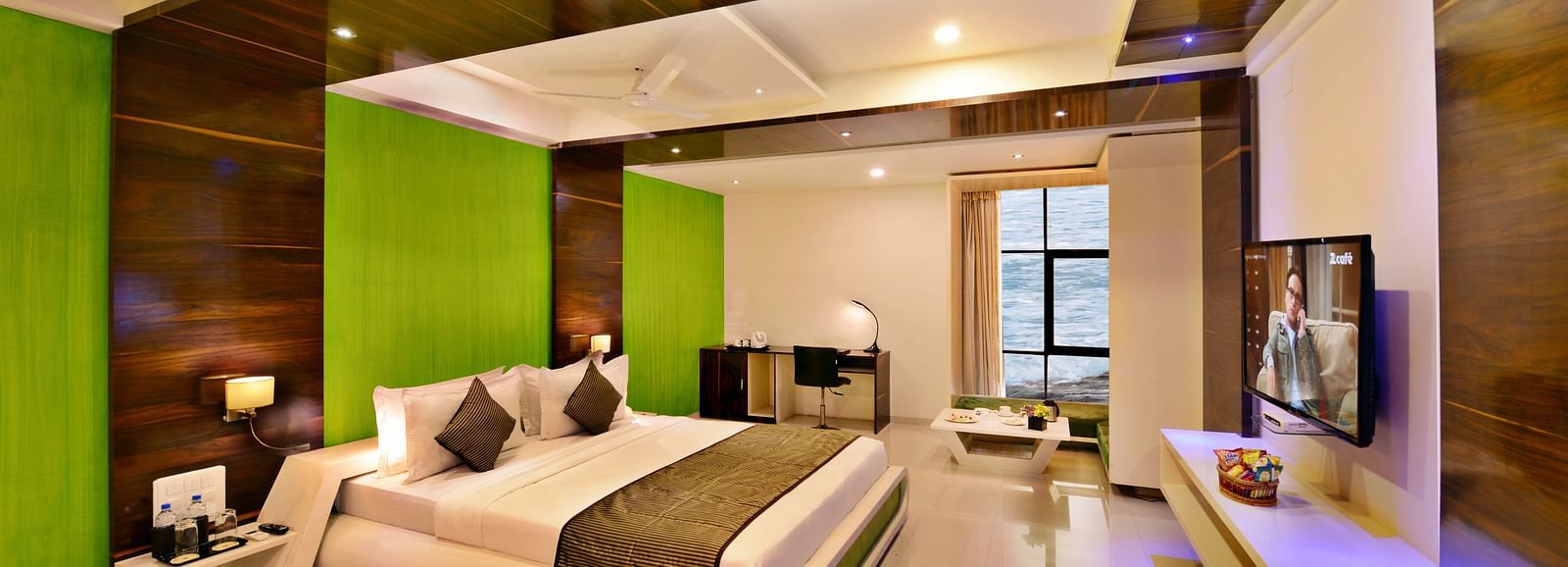 A contemporary hotel suite with a king size bed, green accent wall, and city view.