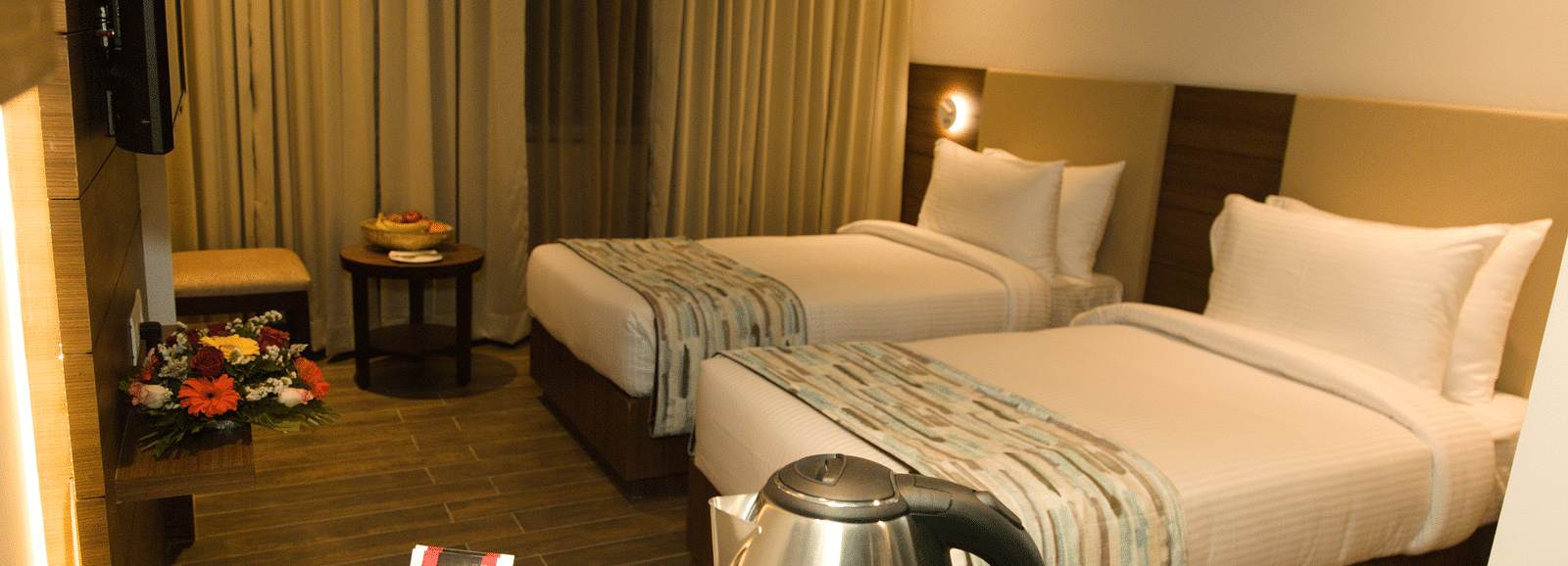 A hotel room at Lords Inn Udaipur offers two single beds with white linens, a kettle, cups, and tea bags on a counter.