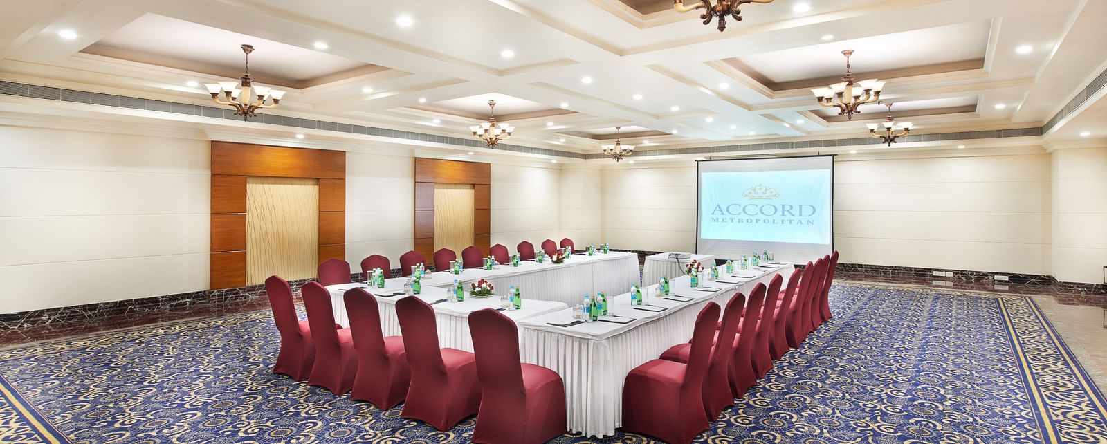 An image of a banquet hall with several chairs and a round table, and a ceiling light hanging from above - Accord Hotels and Resorts