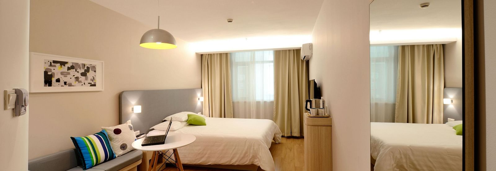 A bright hotel suite includes a seating area and a bed, reflected in a large mirror.