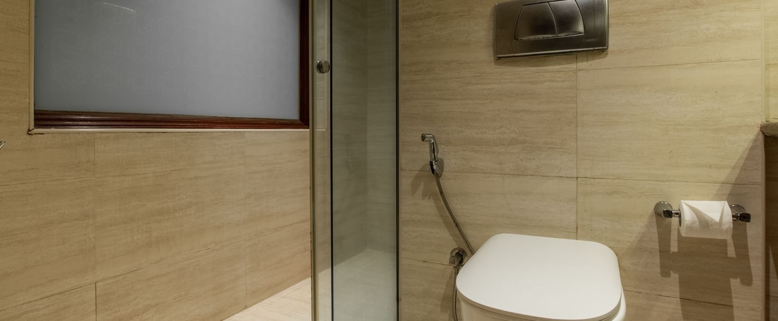 Bathroom with glass shower enclosure, toilet, and tiled walls at Hotel Royal Regency Chennai