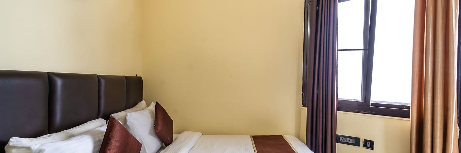 a bed placed by an open window at Flutter Hotels & Resorts
