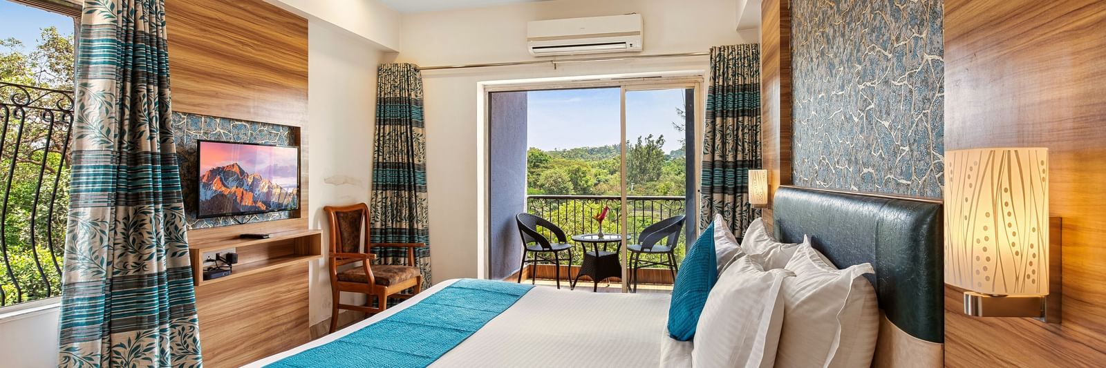Comfortable bedroom at Mayur Retreat with natural light, blue curtains, and a view of the greenery outside.