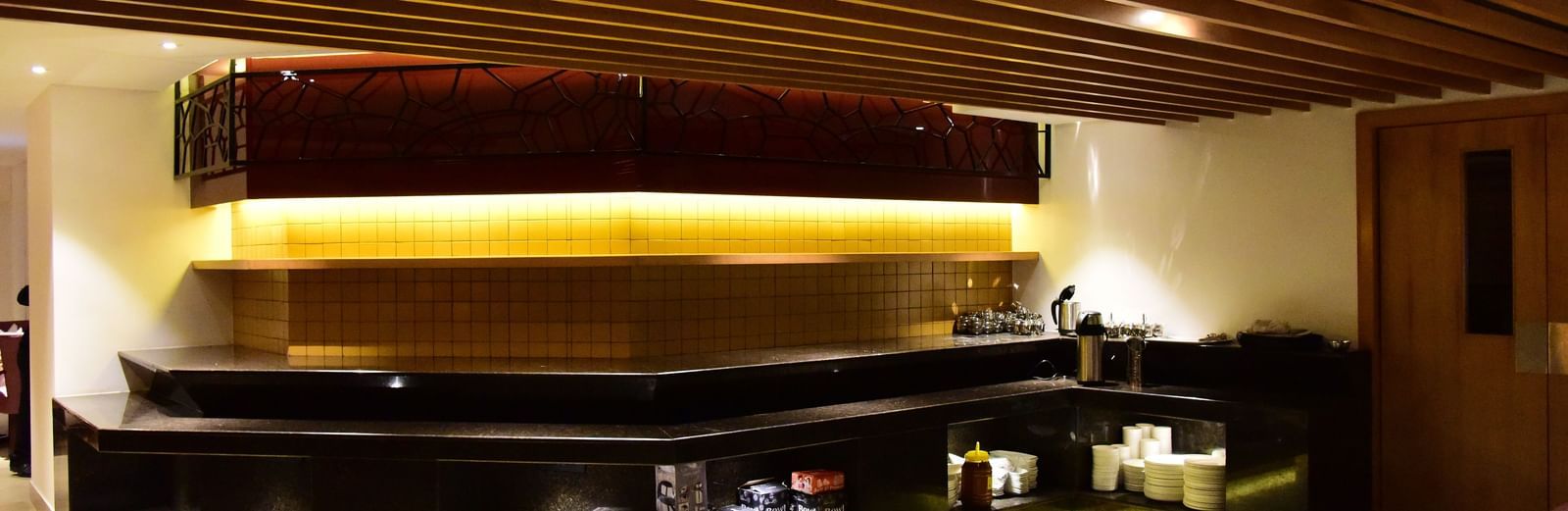 A long shot of the elegant restaurant and bar area at The Royal Comfort, showcasing a long bar with accent lighting and a cosy dining space with tables set for guests.