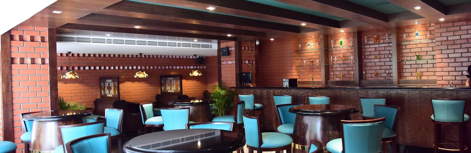 A close-up of the bar area at The Royal Comfort, with wooden rafters on the ceiling and a focus on the blue-green seating and intricate lighting fixtures.