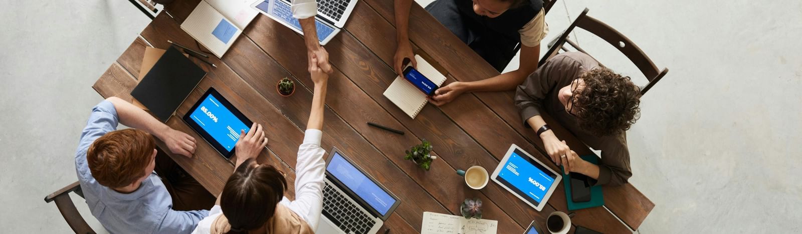 Overhead view of a diverse group of people collaborating around a table with laptops and tablets in an office setting.