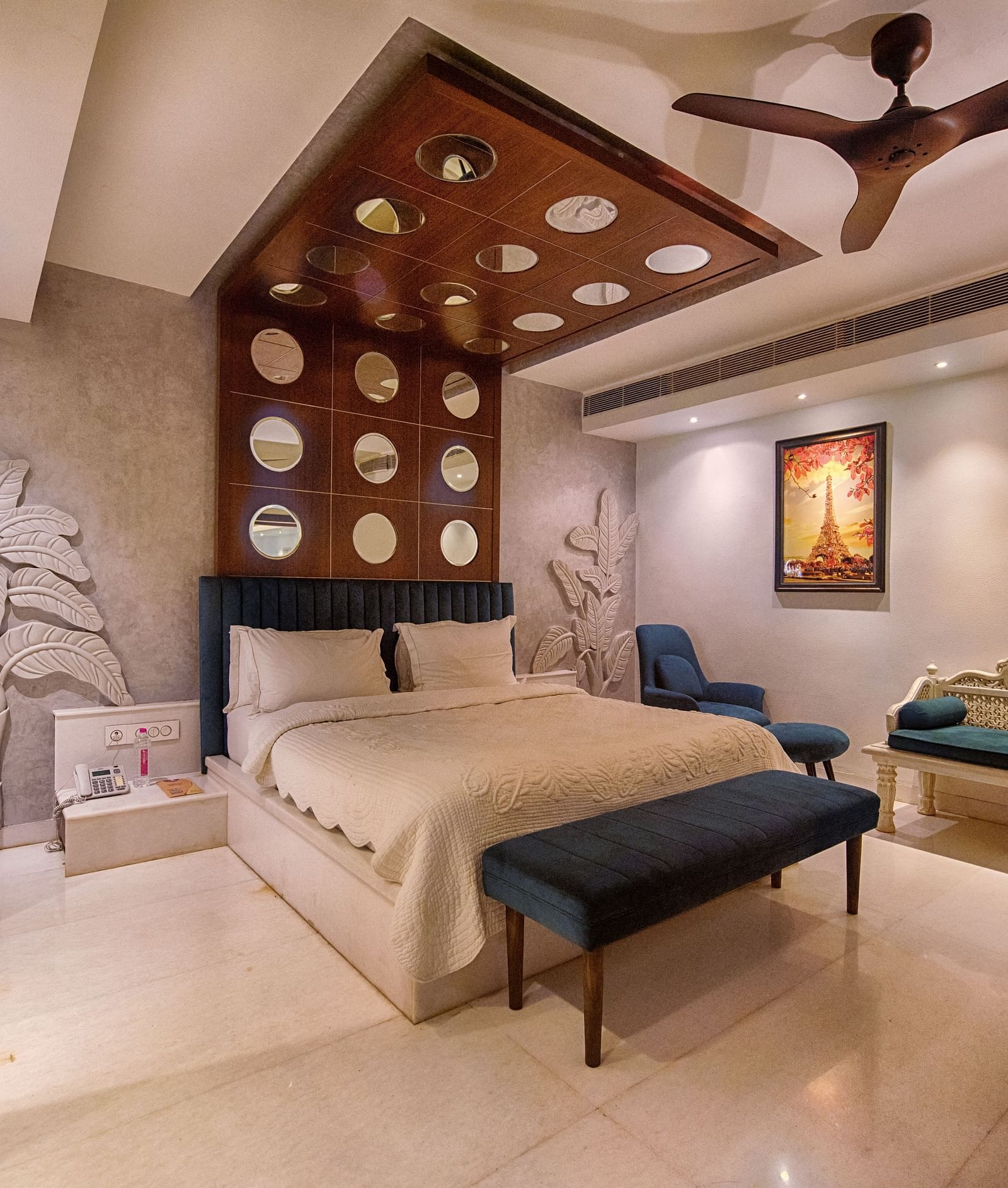 A classy bedroom with a double bed, a cushioned seating for two people, alongside intricate wall sculpts and other decors - Crescent Resorts