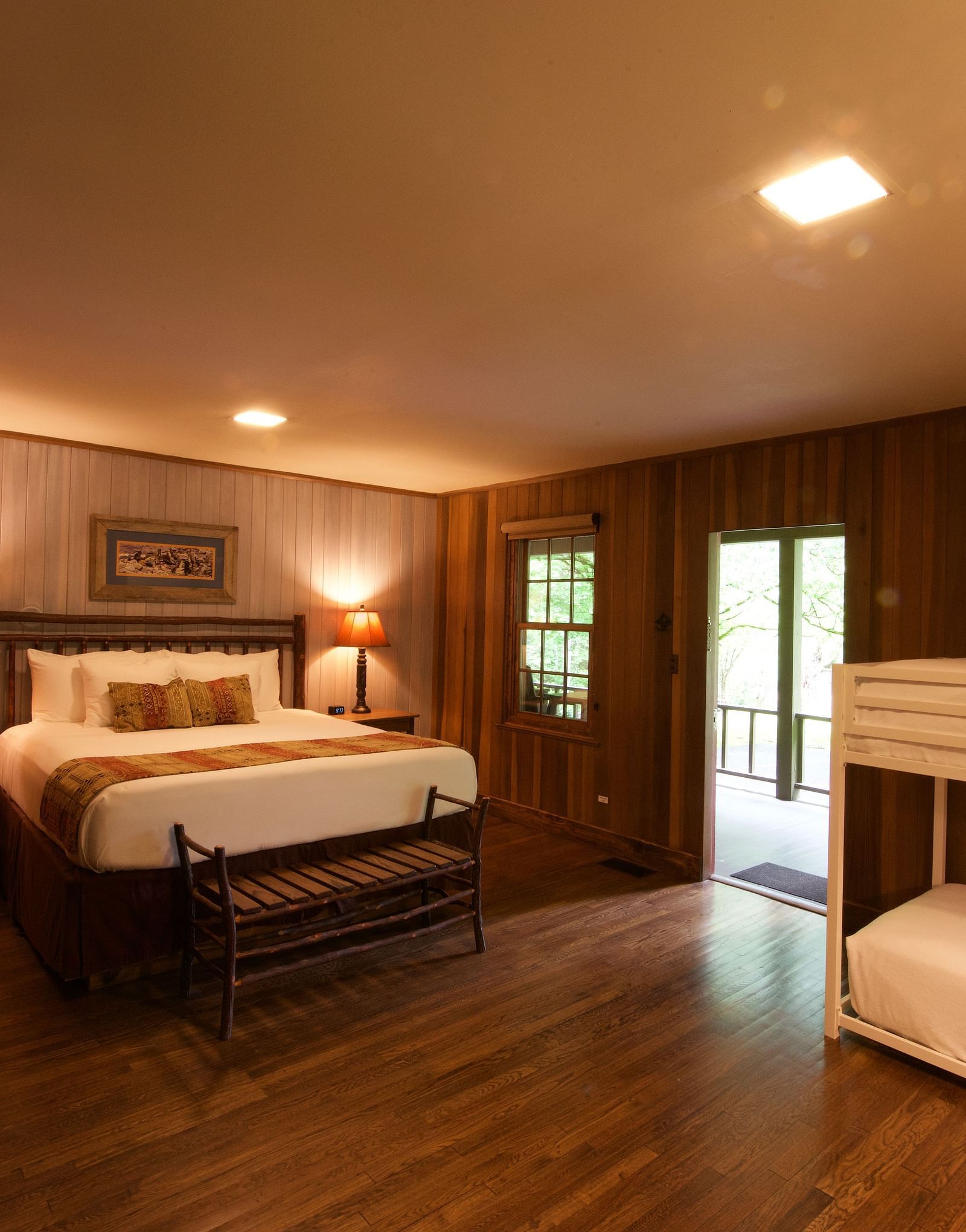 a dimly lit room featuring a double bed along with a bunk bed in the corner with a door opening to the exterior of the cabin - Historic Tapoco Lodge