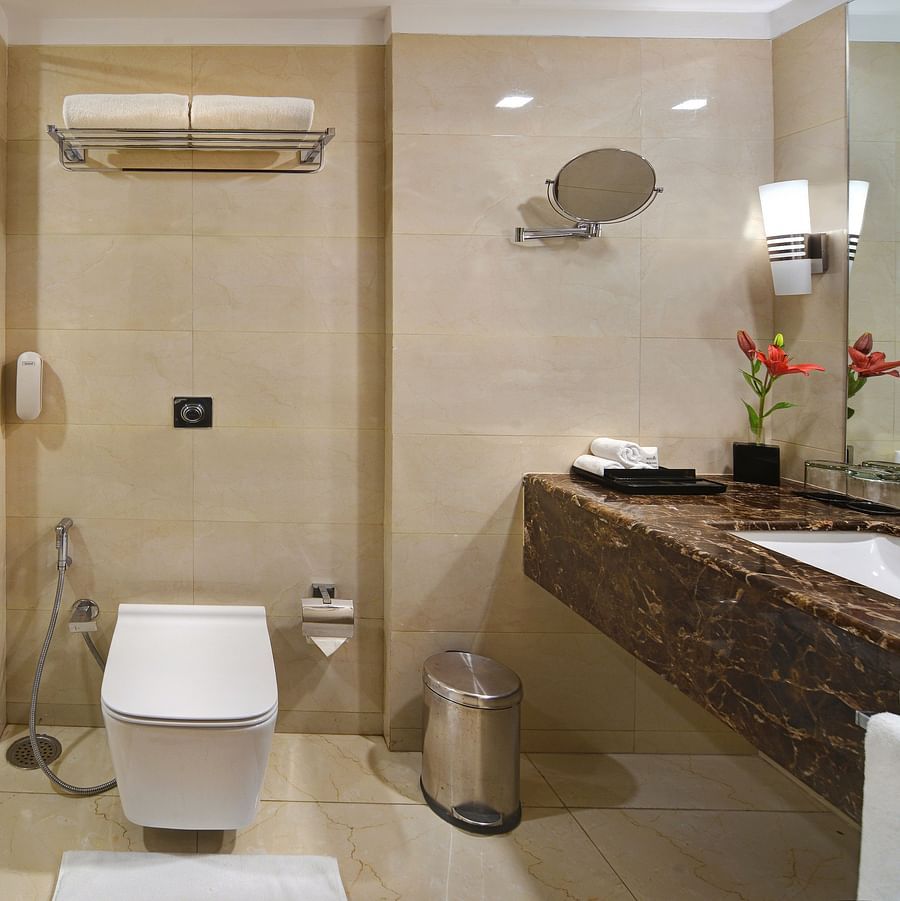 Modern bathroom with glass-enclosed shower, wall-mounted toilet, and elegant vanity at The Bristol Hotel, Gurgaon.