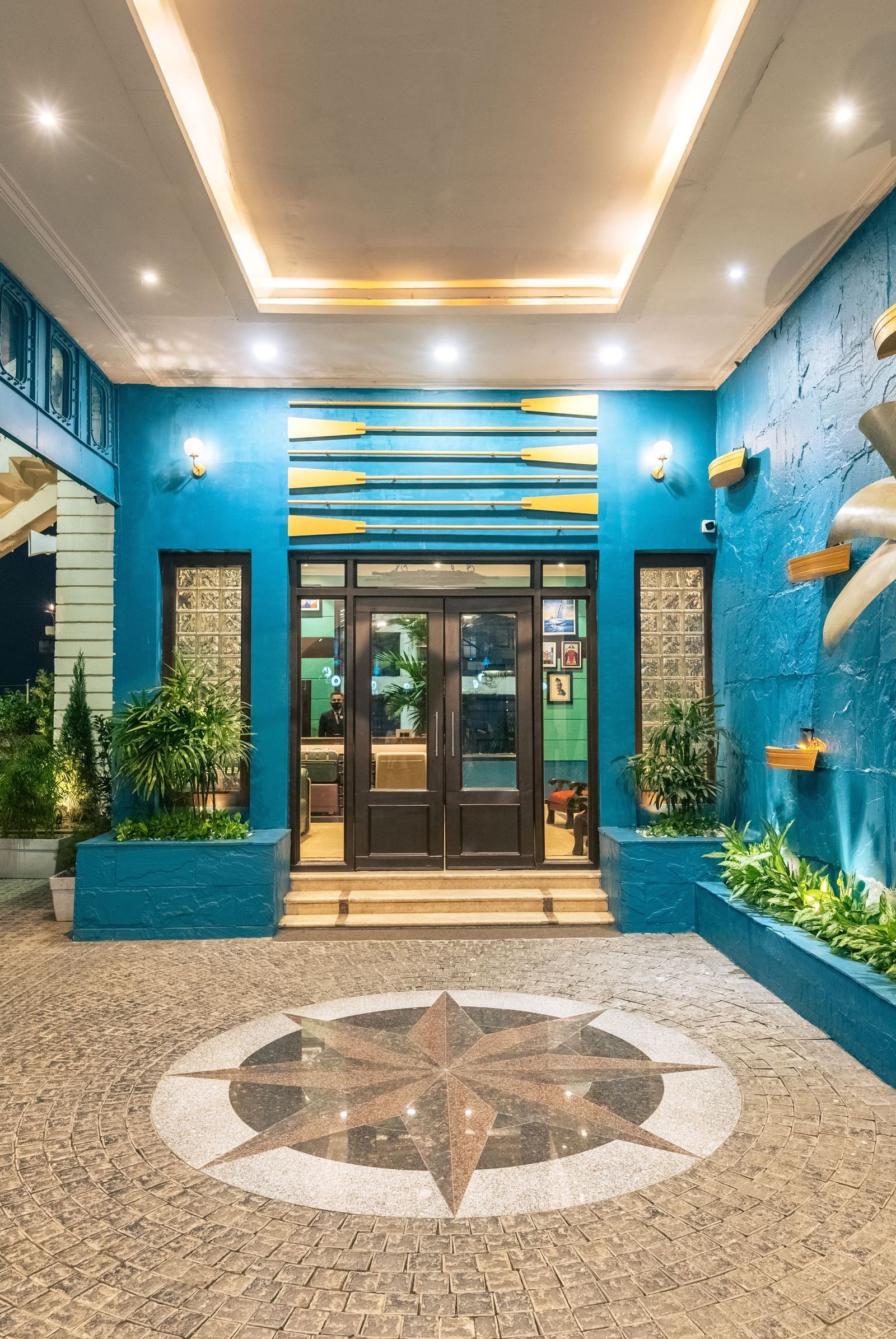 Vibrant hotel entrance at Polo Floatel Kolkata with blue walls, decorative lighting, and a landscaped pathway.